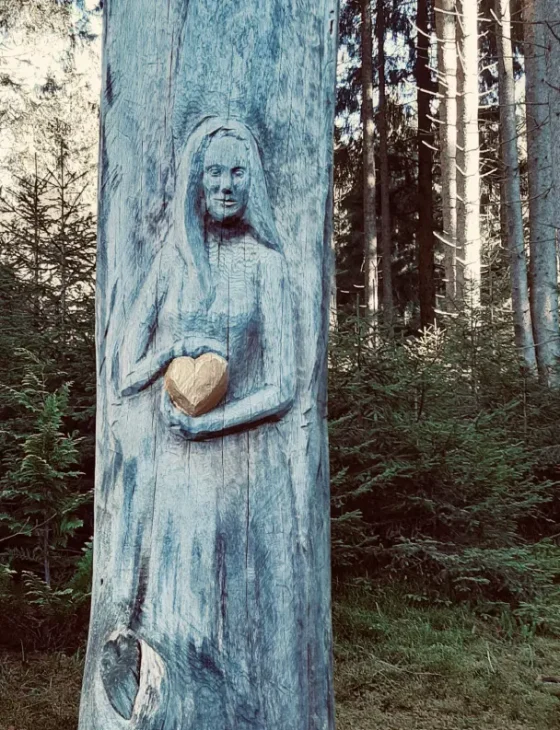 Schnitzfigur Frau auf Baumstamm mit goldenem Herz Lenggries Traumaarbeit